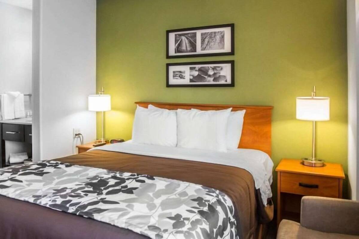 A hotel room with a bed, two bedside lamps, a nightstand, a chair, and two framed pictures on the wall.