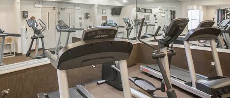 A gym with treadmills, ellipticals, and a mirrored wall.