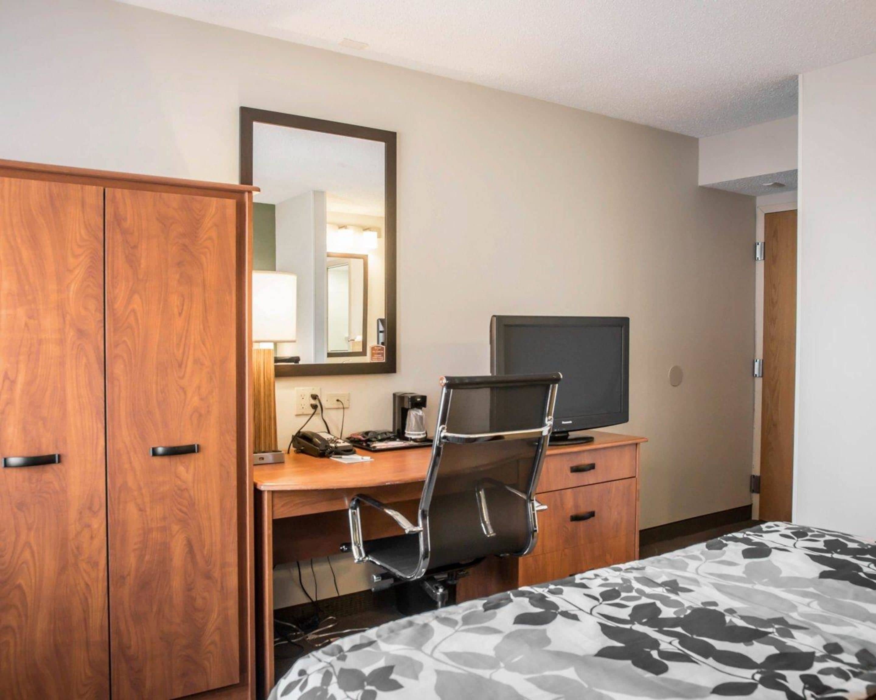 A hotel room with a wooden wardrobe, a desk with a chair, a television, and a bed with a patterned bedspread.