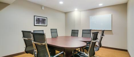 A conference room with a large oval table, six chairs, a whiteboard, and a framed picture on the wall.