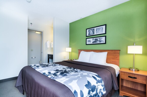 A hotel room with a bed, two bedside lamps, a wooden nightstand, and two framed pictures on the green wall. - Sleep Inn Midway Airport Bedford Park (Chicago)