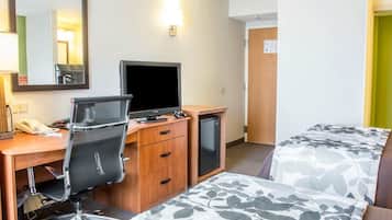 A hotel room with a desk, a chair, a bed with floral bedding, a television, and a small refrigerator.