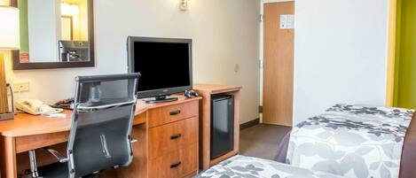 A hotel room with a desk, a chair, a bed with floral bedding, a television, and a small refrigerator.