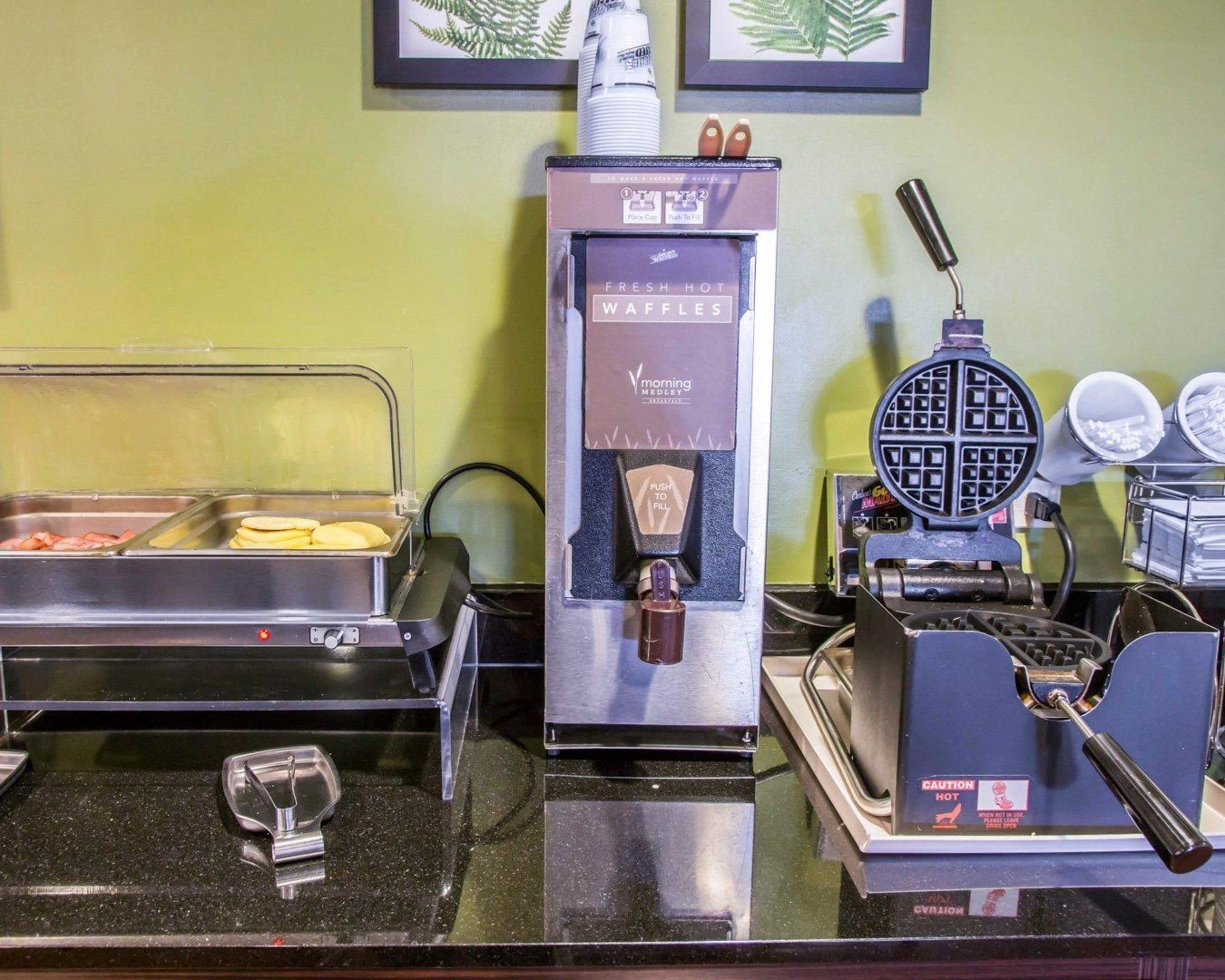 A buffet setup with a waffle maker, a hot food dispenser, and a tray of food items.