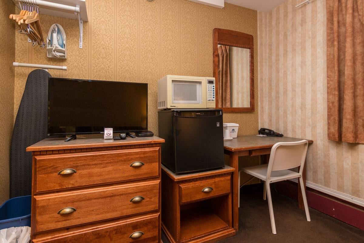 Une chambre d’hôtel de taille modeste, comprenant une commode en bois, un téléviseur, un four à micro-ondes, un réfrigérateur, un bureau et une chaise.