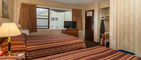 Ein Hotelzimmer mit zwei Betten, einem Fernseher, einem Schreibtisch und einem Fenster mit Vorhängen.