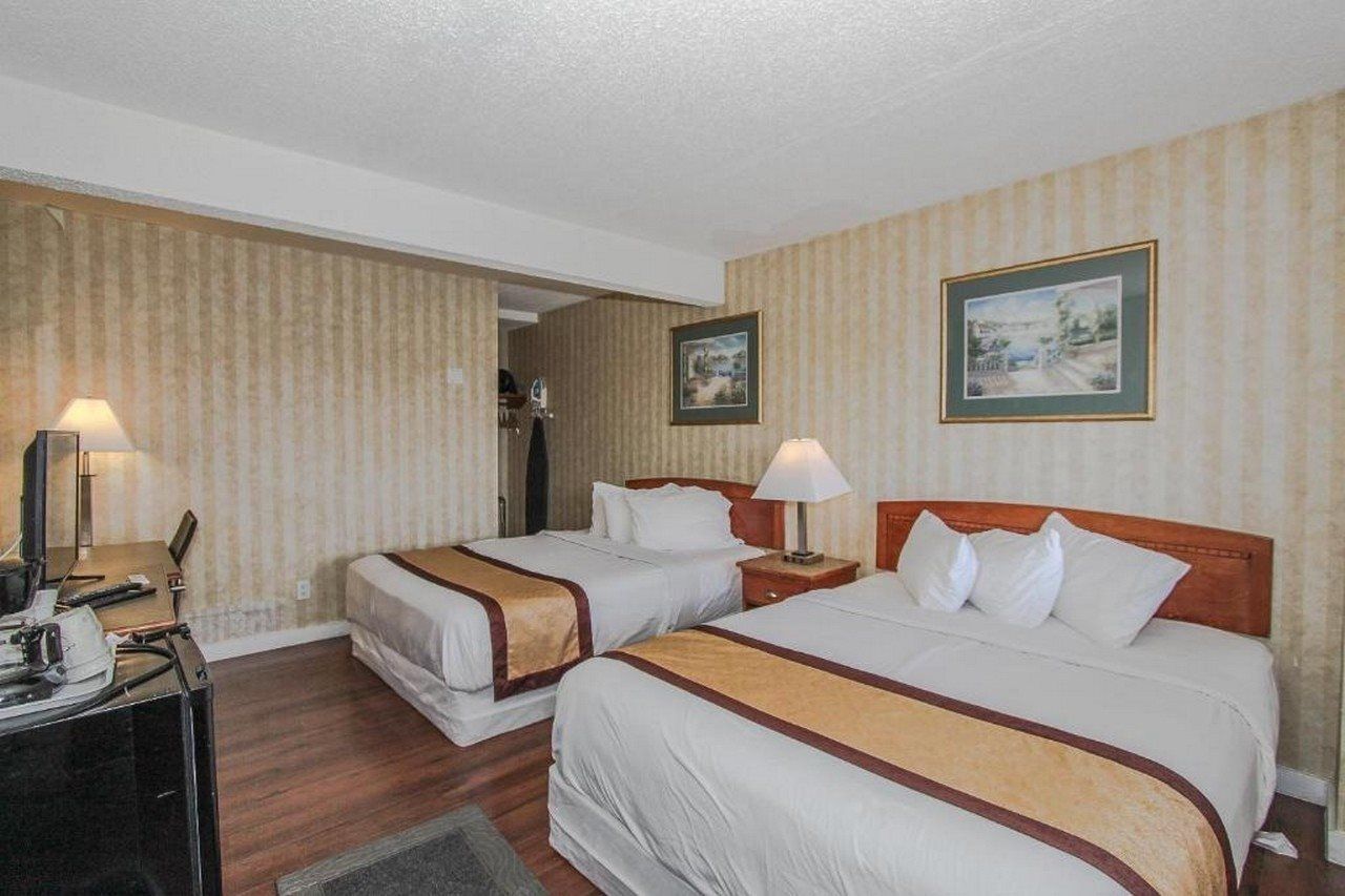 Une chambre d’hôtel avec deux lits, un bureau et une chaise. Il y a deux lampes sur le bureau et un tableau encadré au mur.