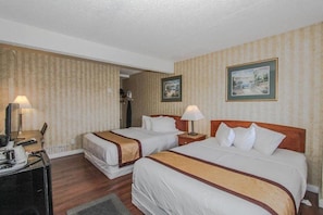 Une chambre d’hôtel avec deux lits, un bureau et une chaise. Il y a deux lampes sur le bureau et un tableau encadré au mur.