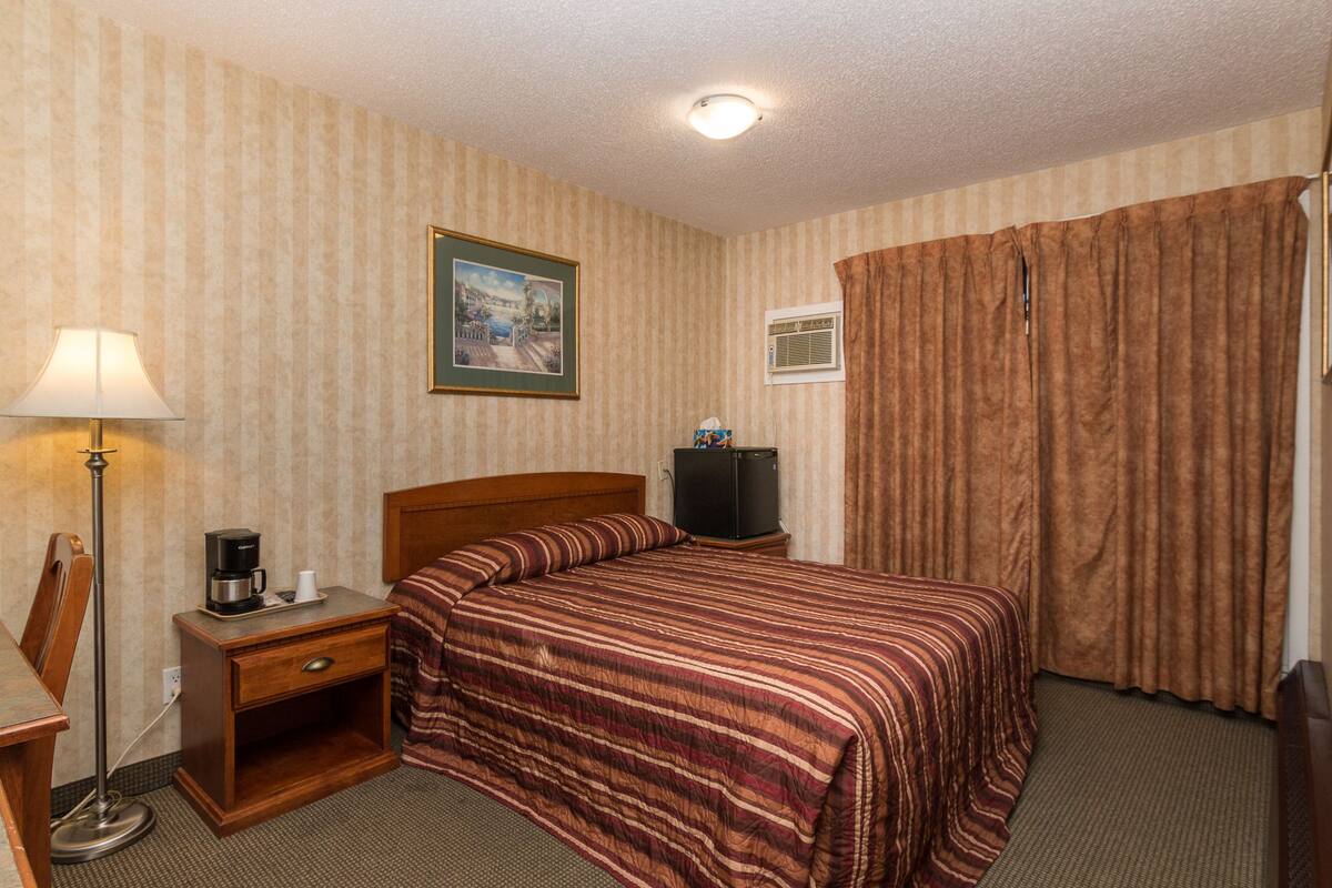 Une chambre d’hôtel avec un lit, un bureau avec une lampe, une machine à café, une télévision et des rideaux.