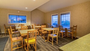 A dining area with wooden tables and chairs, large windows, and a clock on the wall.