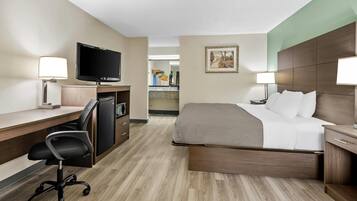 Habitación de hotel con cama, escritorio, silla, televisor y baño visible al fondo.