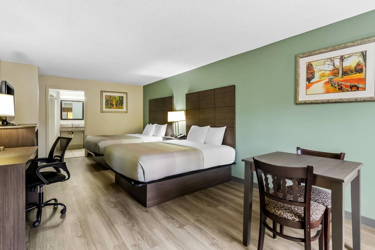 A hotel room with a bed, desk, chair, and a painting on the wall.