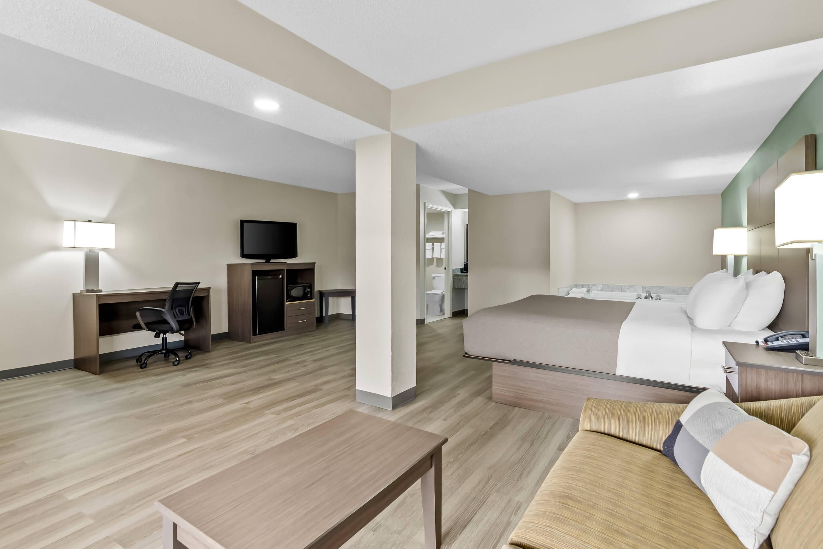 Une chambre d’hôtel avec un lit, un bureau et une chaise, une télévision et une salle de bain visible à travers une porte ouverte.