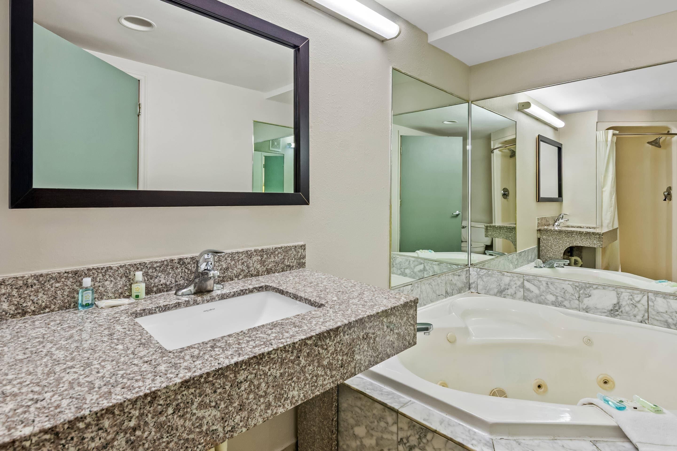 A bathroom with a granite countertop sink, a large mirror, a bathtub, and a shower area.