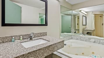 Un baño con lavamanos de encimera de granito, un espejo grande, bañera y zona de ducha.