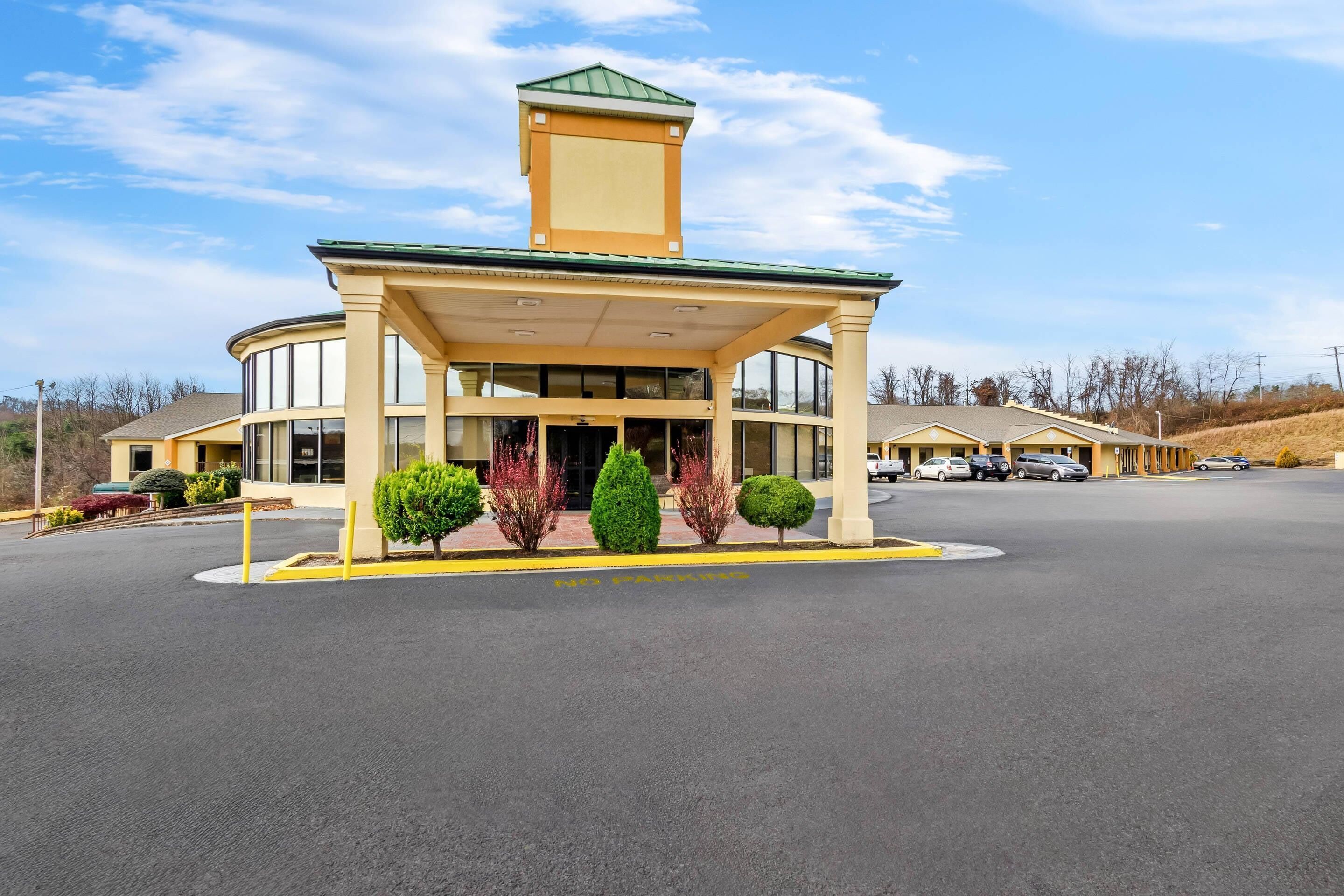 A hotel with a central entrance, a covered waiting area, and a parking lot.