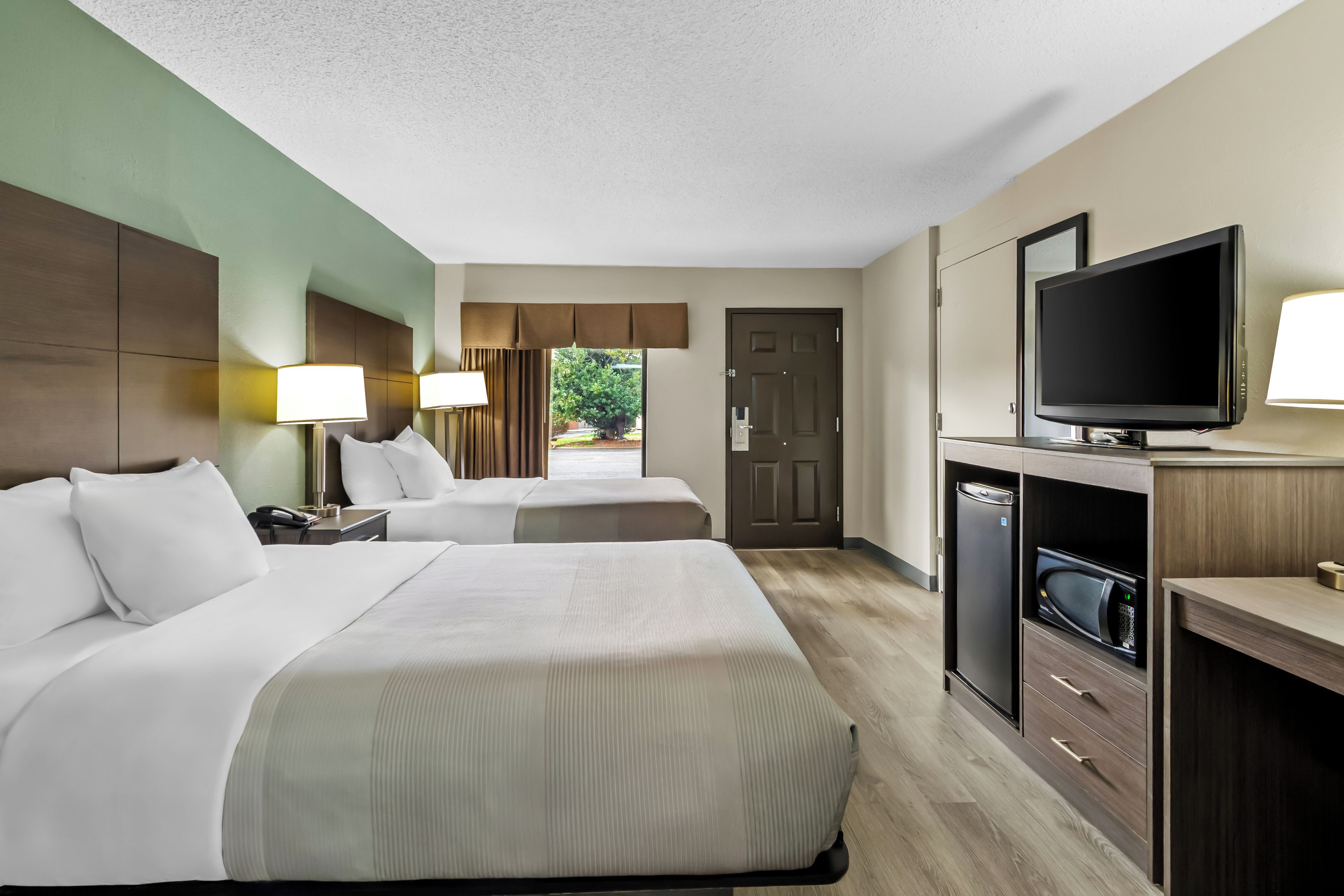 A hotel room with two beds, a television, a desk, and a view of the outdoors.