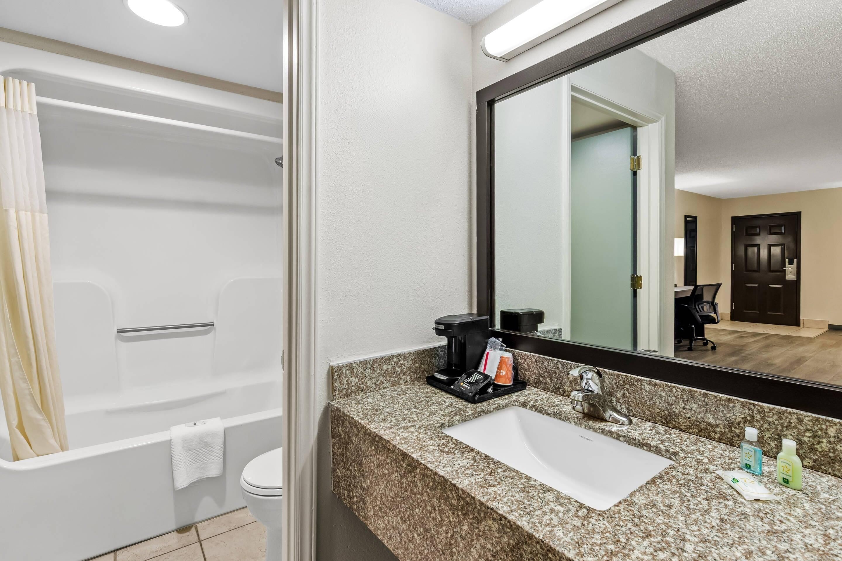 A modern bathroom with a bathtub, a sink with toiletries, and a large mirror.