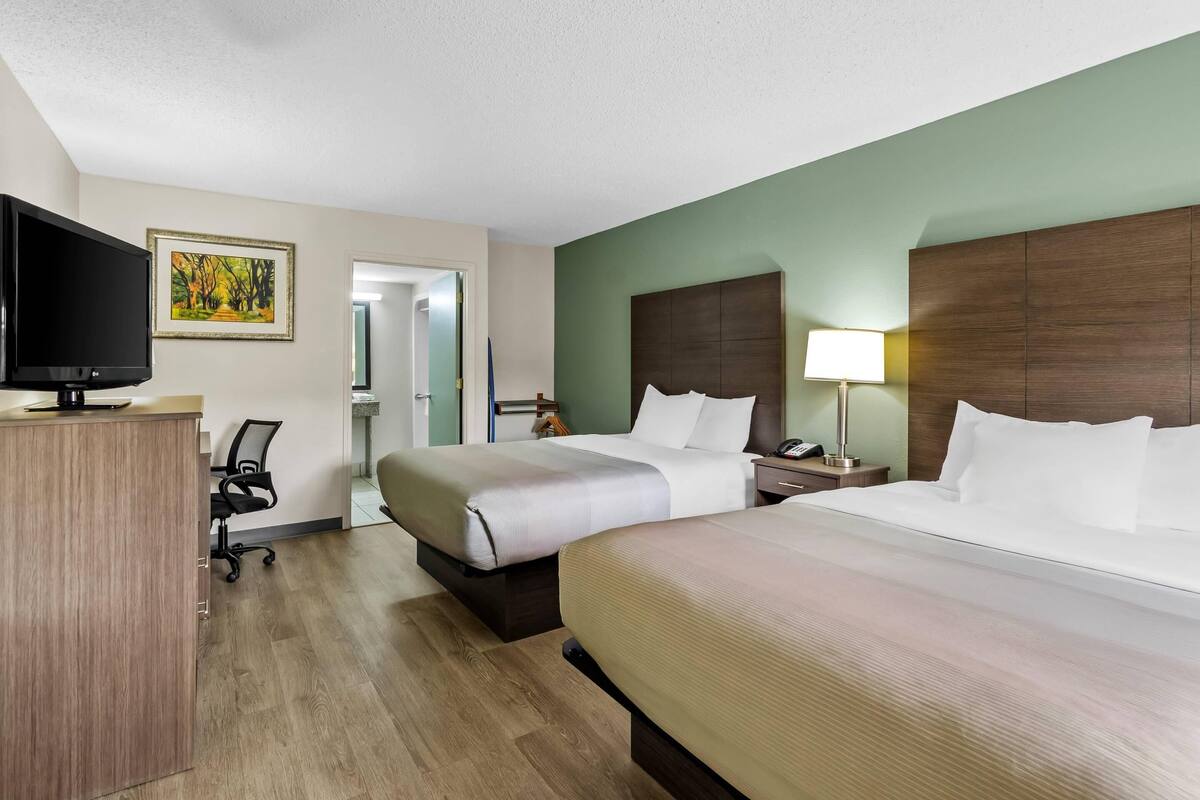 A hotel room with two beds, a desk with a TV, a chair, and a painting on the wall.