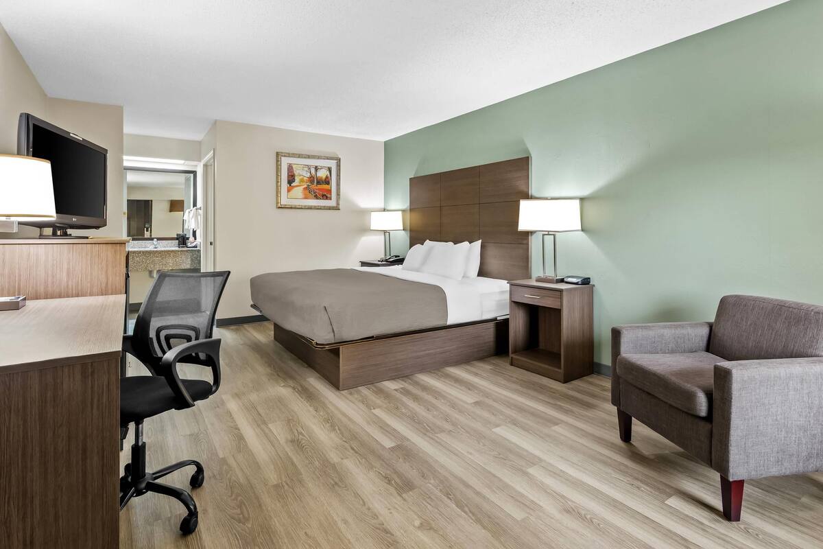 A hotel room with a bed, desk, chair, TV, and a painting on the wall.