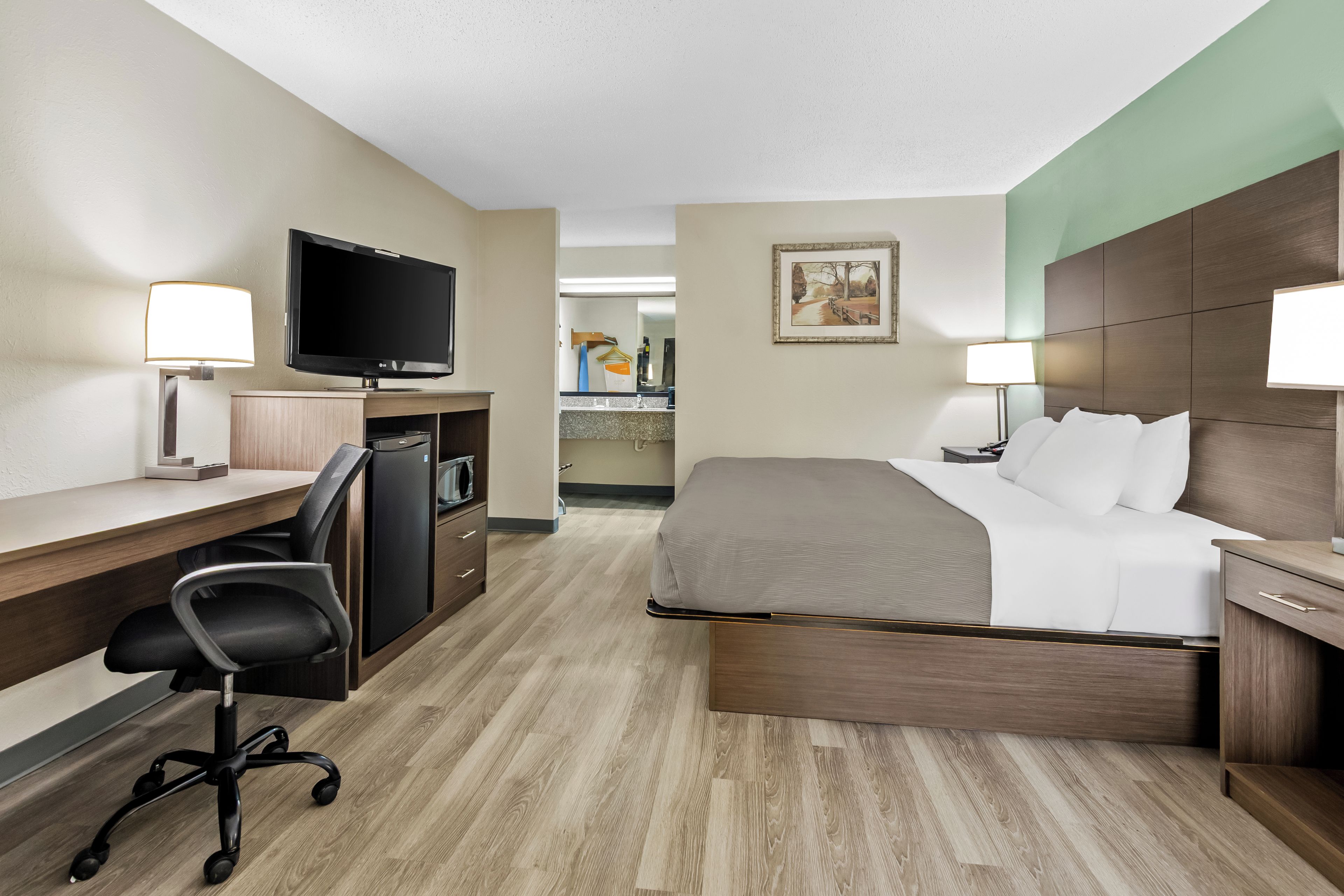 A hotel room with a bed, desk, chair, television, and a painting on the wall.