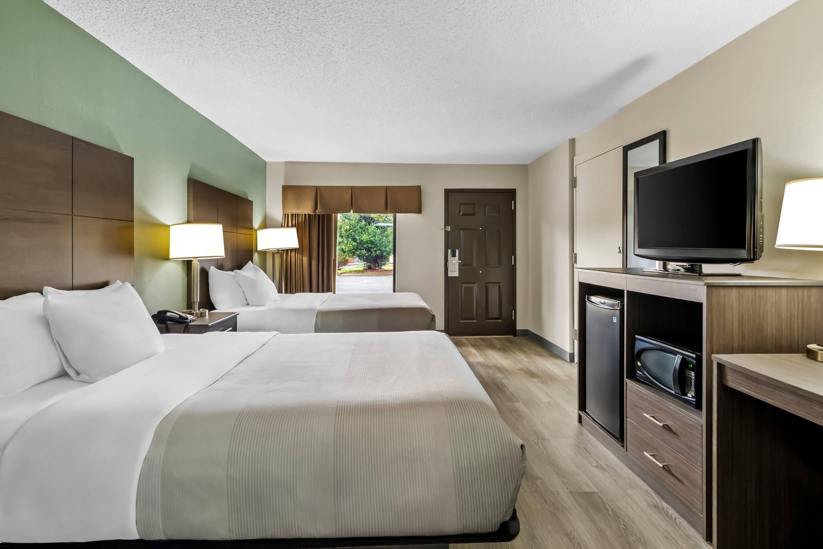 A hotel room with two beds, a TV, a microwave, and a refrigerator.