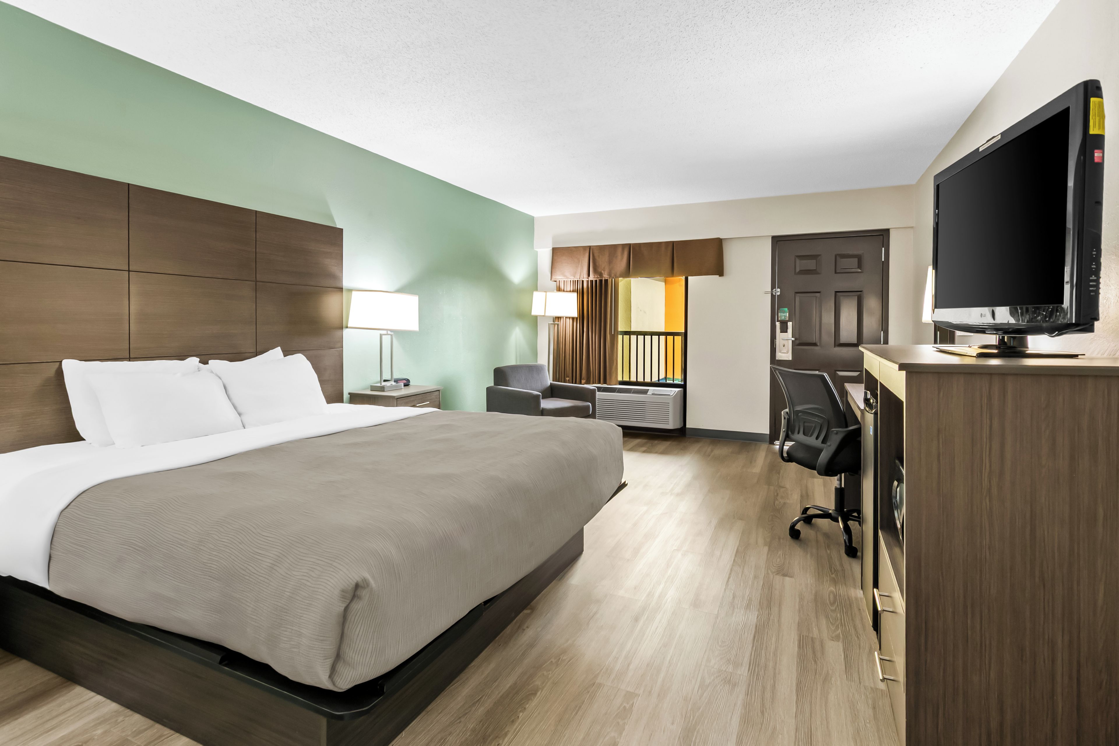 A hotel room with a bed, a desk, a chair, a television, and an air conditioning unit.