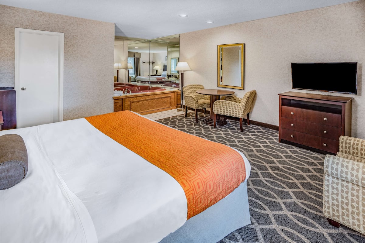 A hotel room with a bed, a desk, a chair, a television, and a bathroom visible through a mirror.