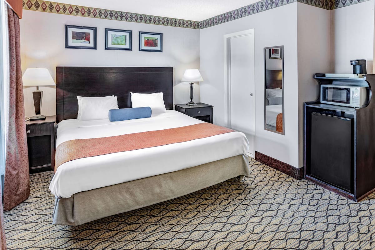 A hotel room with a large bed, bedside lamps, a desk with a computer, a microwave, and framed pictures on the wall.
