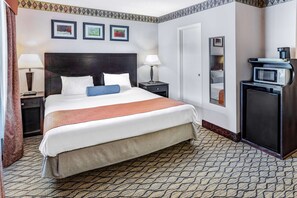 A hotel room with a large bed, bedside lamps, a desk with a computer, a microwave, and framed pictures on the wall. - Howard Johnson by Wyndham Lenox (Lenox)