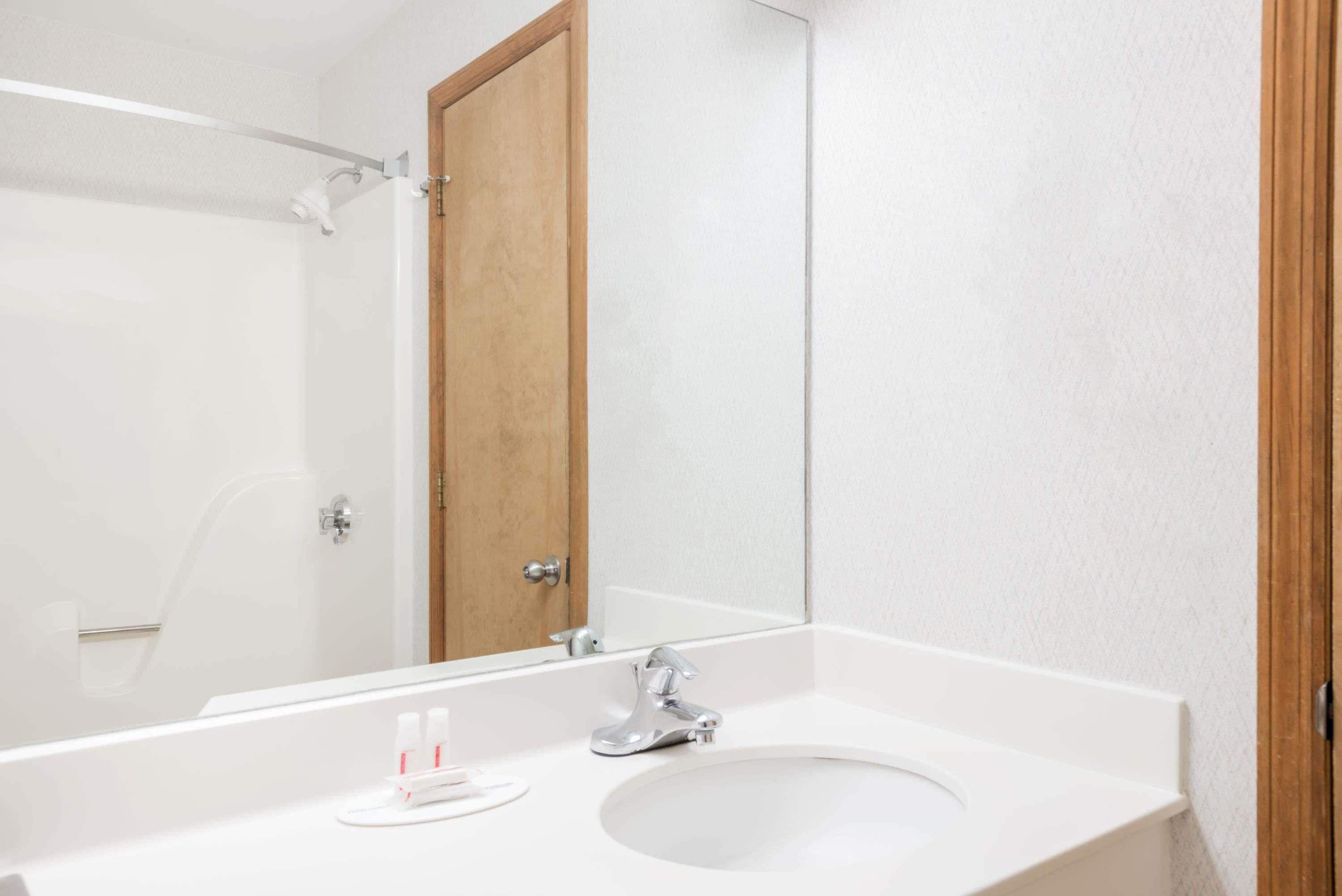 Un baño con un lavamanos blanco, un espejo y una puerta de madera.