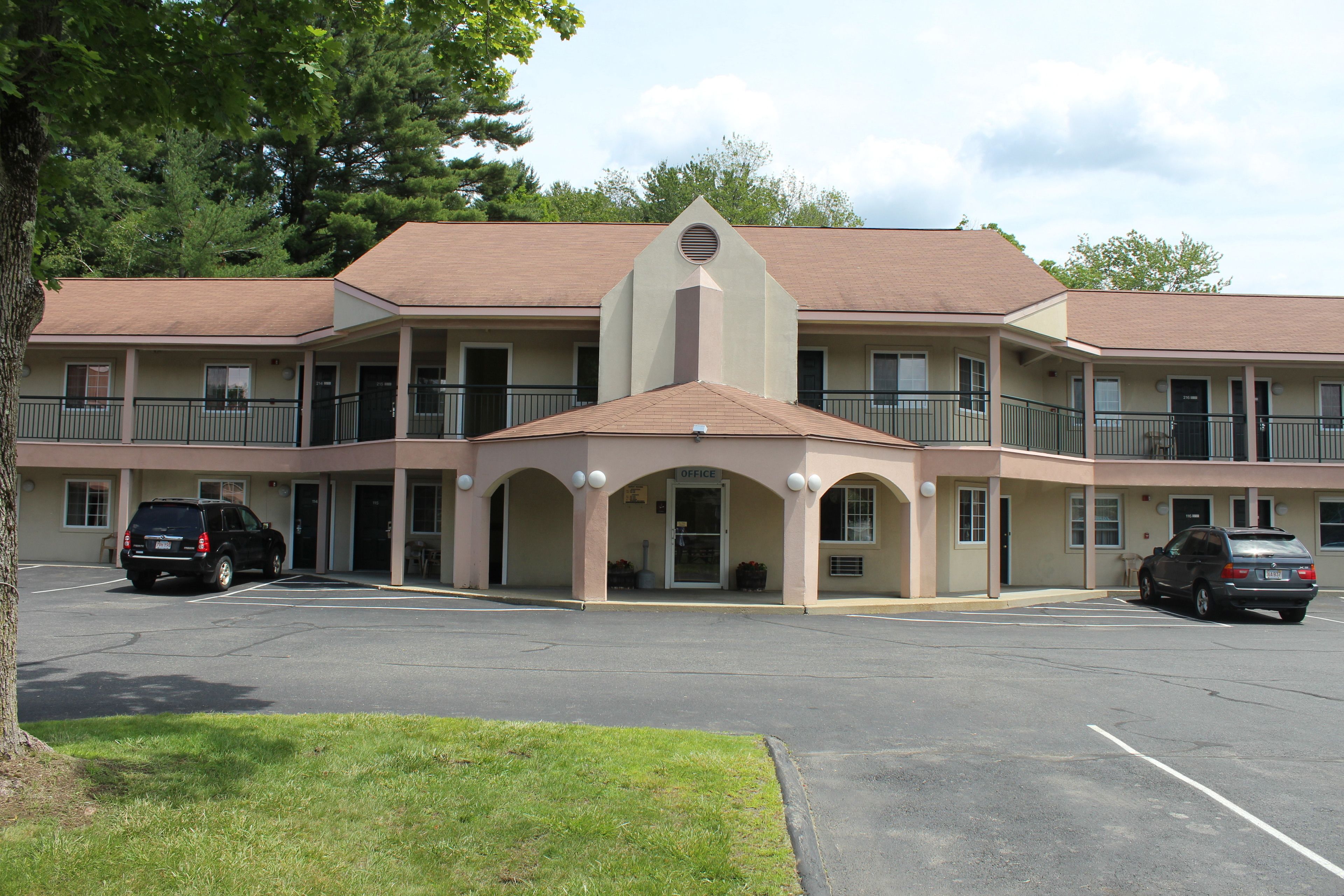 A multi-story motel with a central entrance, parking lot, and a building with balconies.