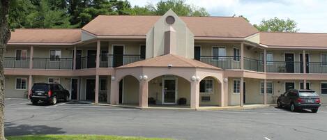 A multi-story motel with a central entrance, parking lot, and a building with balconies.