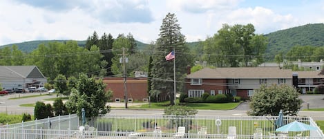 A swimming pool with a white fence, a flag, and a view of a town with houses and a hill in the background.