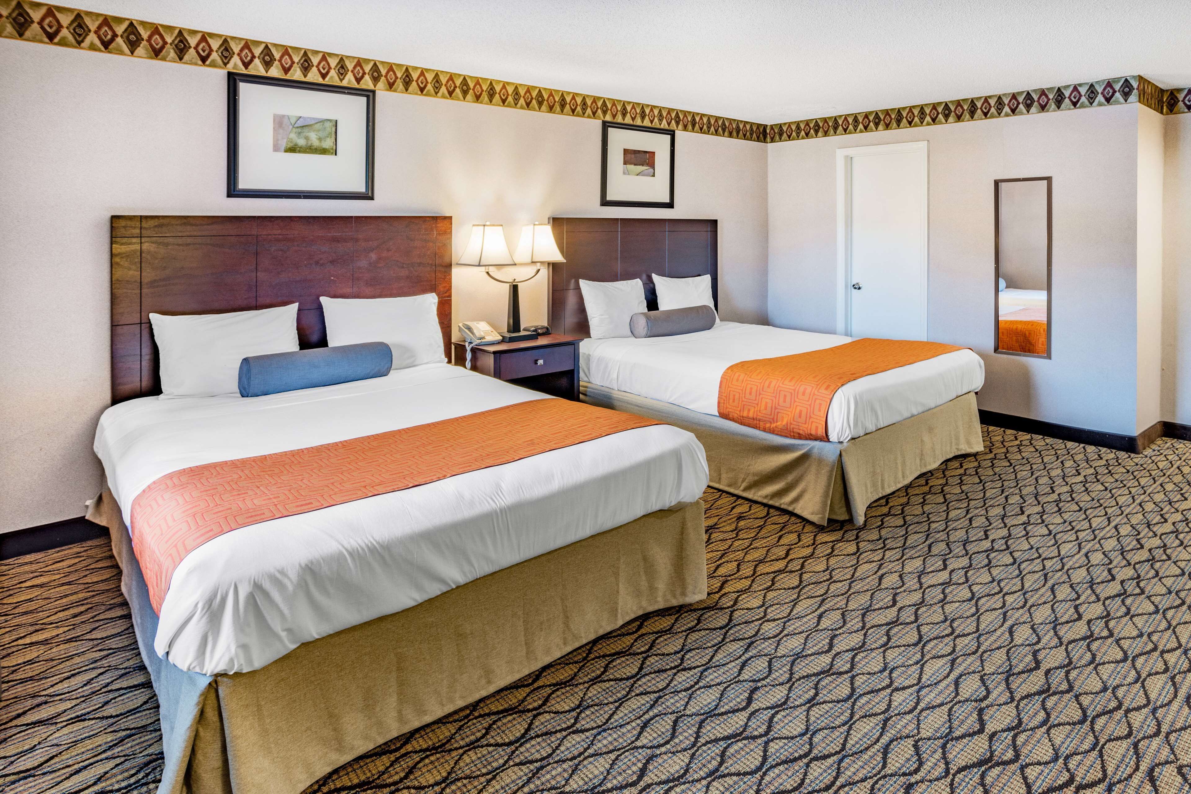 A hotel room with two beds, a nightstand with a lamp, a framed picture on the wall, and a patterned carpet.