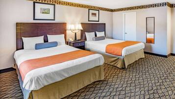 A hotel room with two beds, a nightstand with a lamp, a framed picture on the wall, and a patterned carpet.
