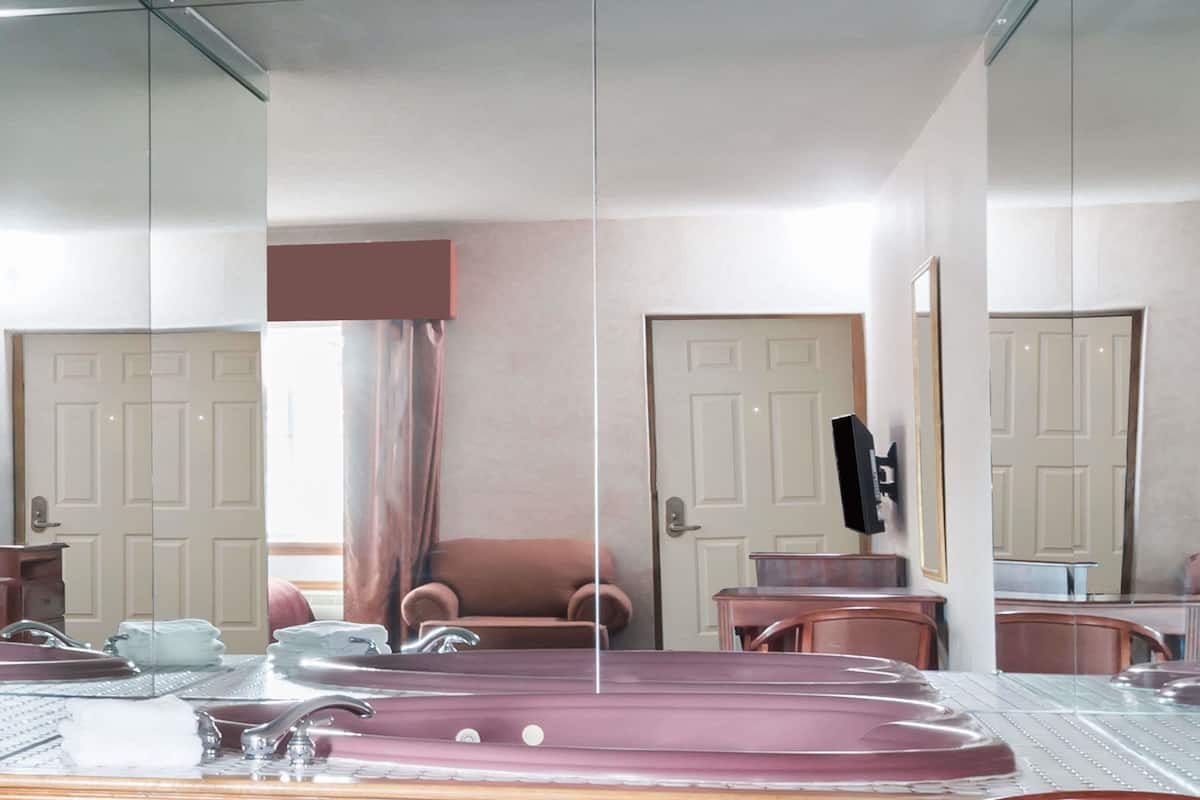 A room with a large mirror, a sofa, a chair, a small table, and a bathtub.
