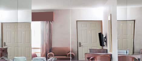 A room with a large mirror, a sofa, a chair, a small table, and a bathtub.