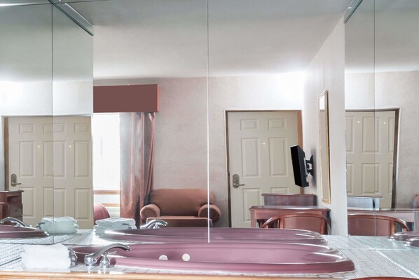 Una habitación con un espejo grande, un sofá, una silla, una mesita y una bañera.