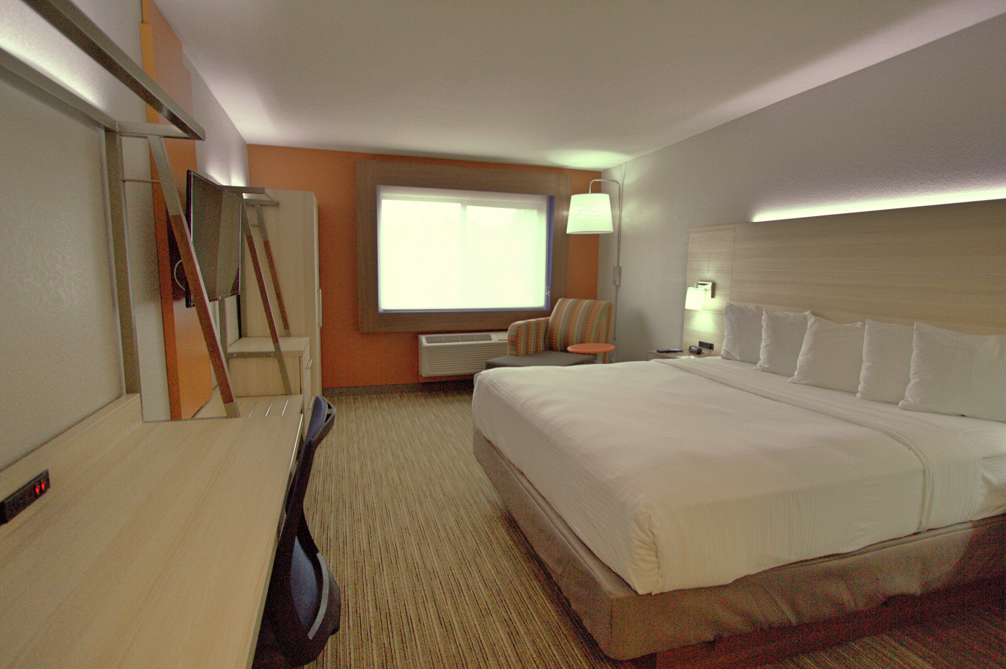 A hotel room with a large bed, a desk, a chair, a TV, and a window.