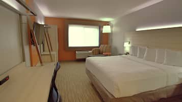 A hotel room with a large bed, a desk, a chair, a TV, and a window.