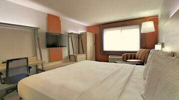 Habitación de hotel con una cama grande, un escritorio con silla, televisión, armario y ventana con vistas.