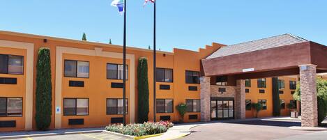 A multi-story hotel with a flat roof, a parking lot with marked handicapped spaces, and a clear sky.