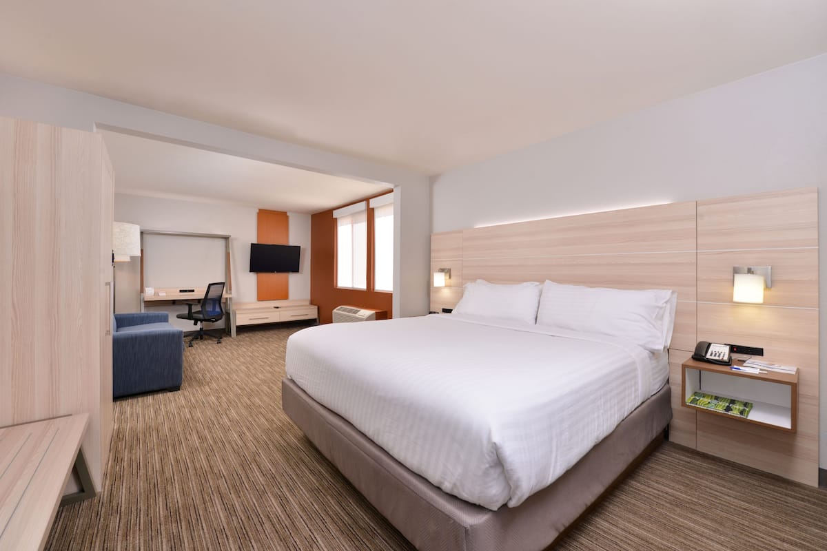 A modern hotel room with a large bed, a desk, a chair, and a TV.