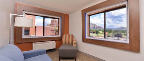 A hotel room with a large window, a sofa, an ottoman, and a lamp.