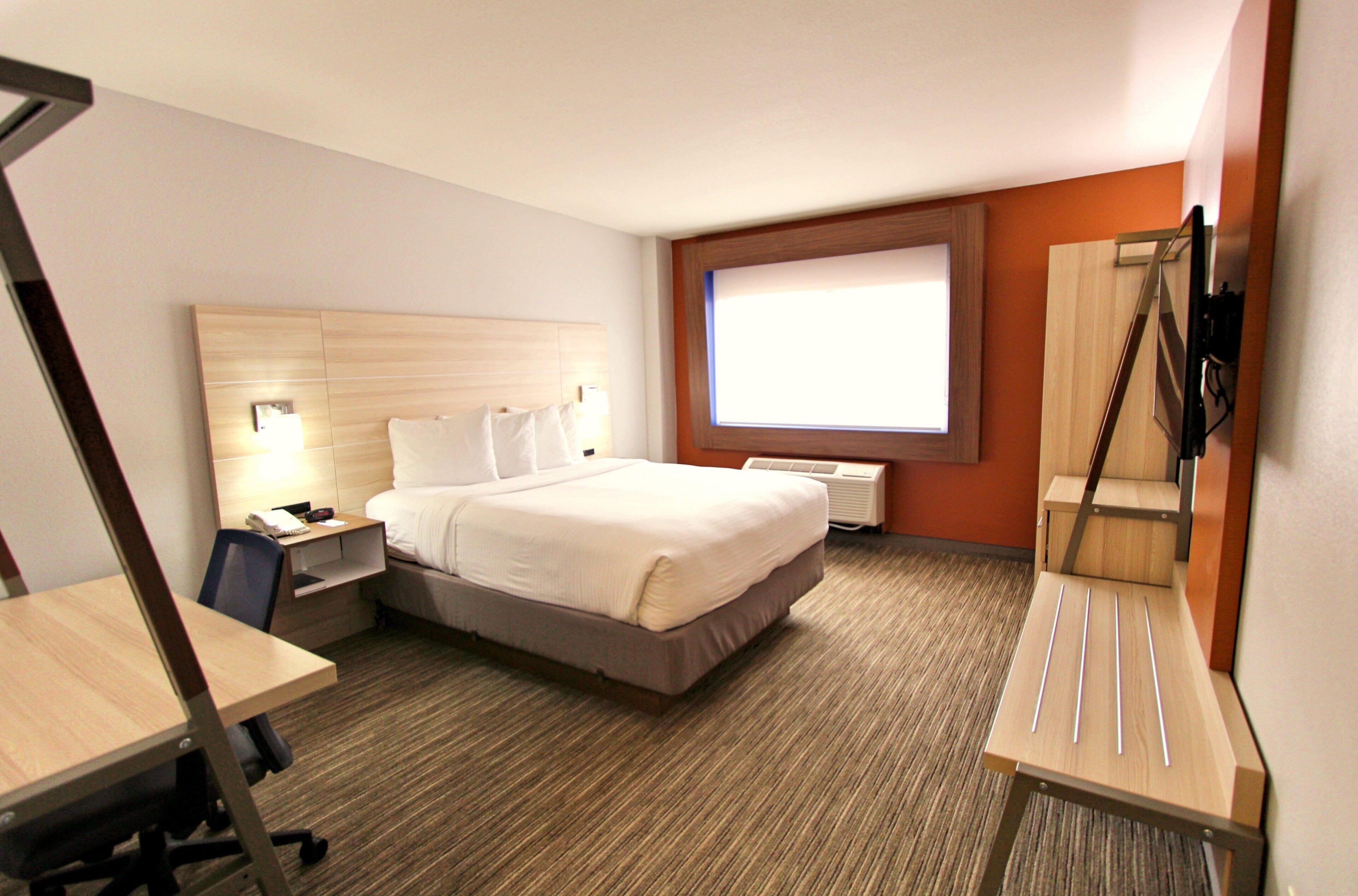Ein Hotelzimmer mit Bett, Nachttisch, Schreibtisch, Stuhl und einem Fenster mit Jalousien.