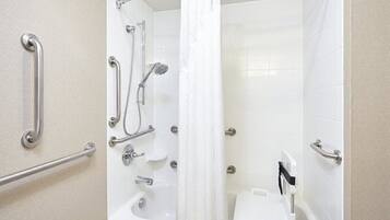 A bathroom with a bathtub, shower, and toilet, equipped with handrails and grab bars.