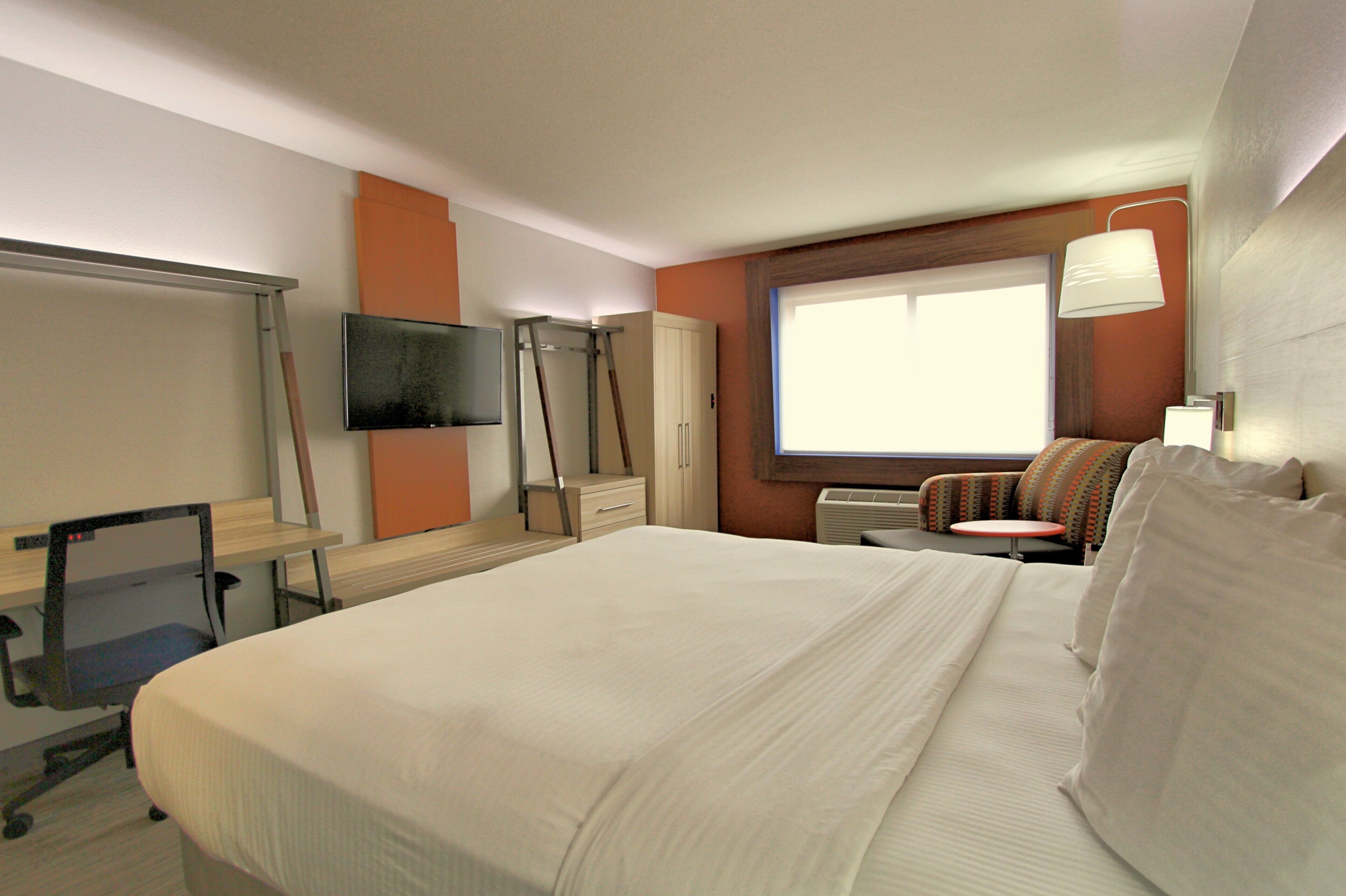 Una habitación de hotel con cama, escritorio, silla, televisor y ventana.