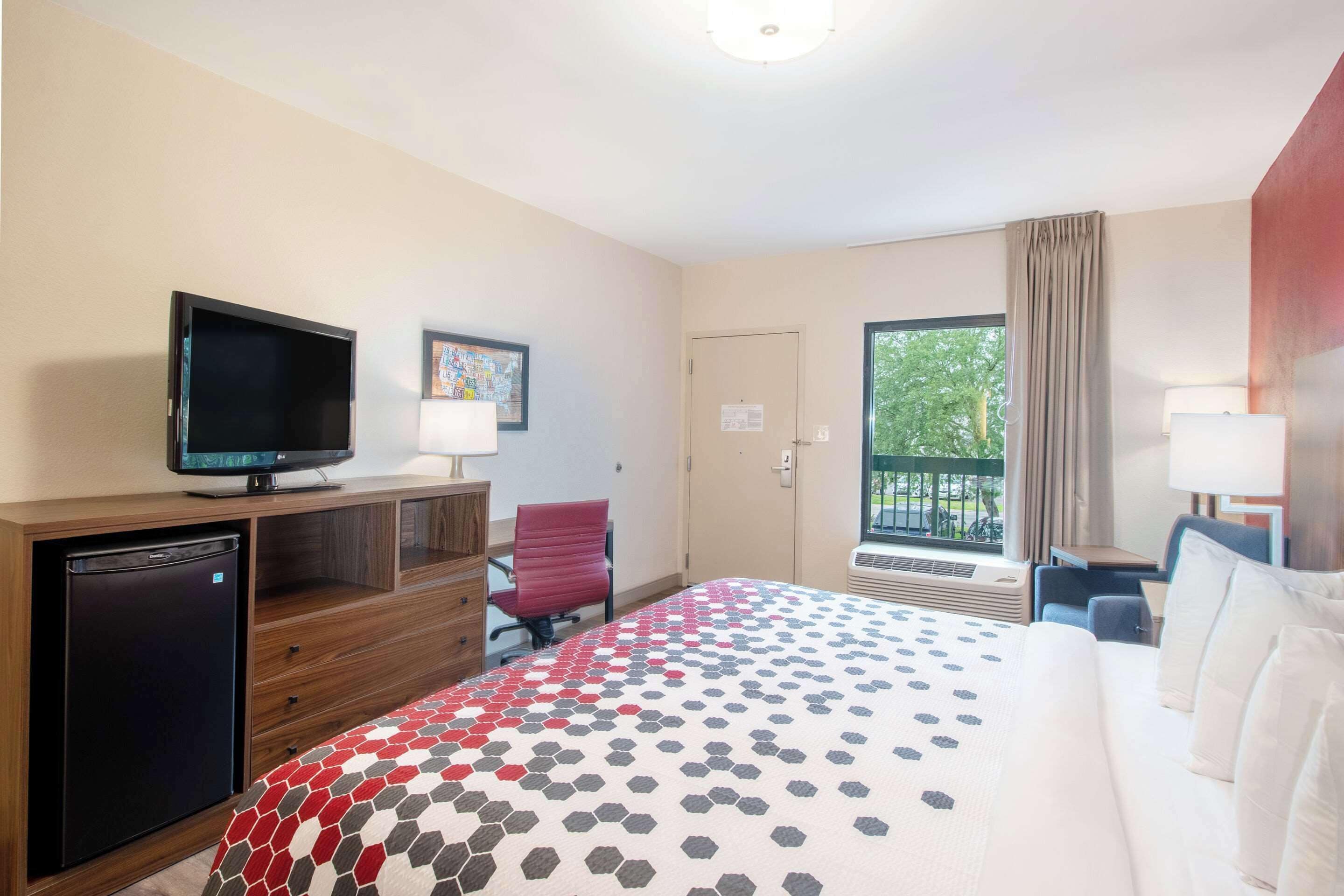 Habitación de hotel con cama, escritorio, silla, televisor y refrigerador.