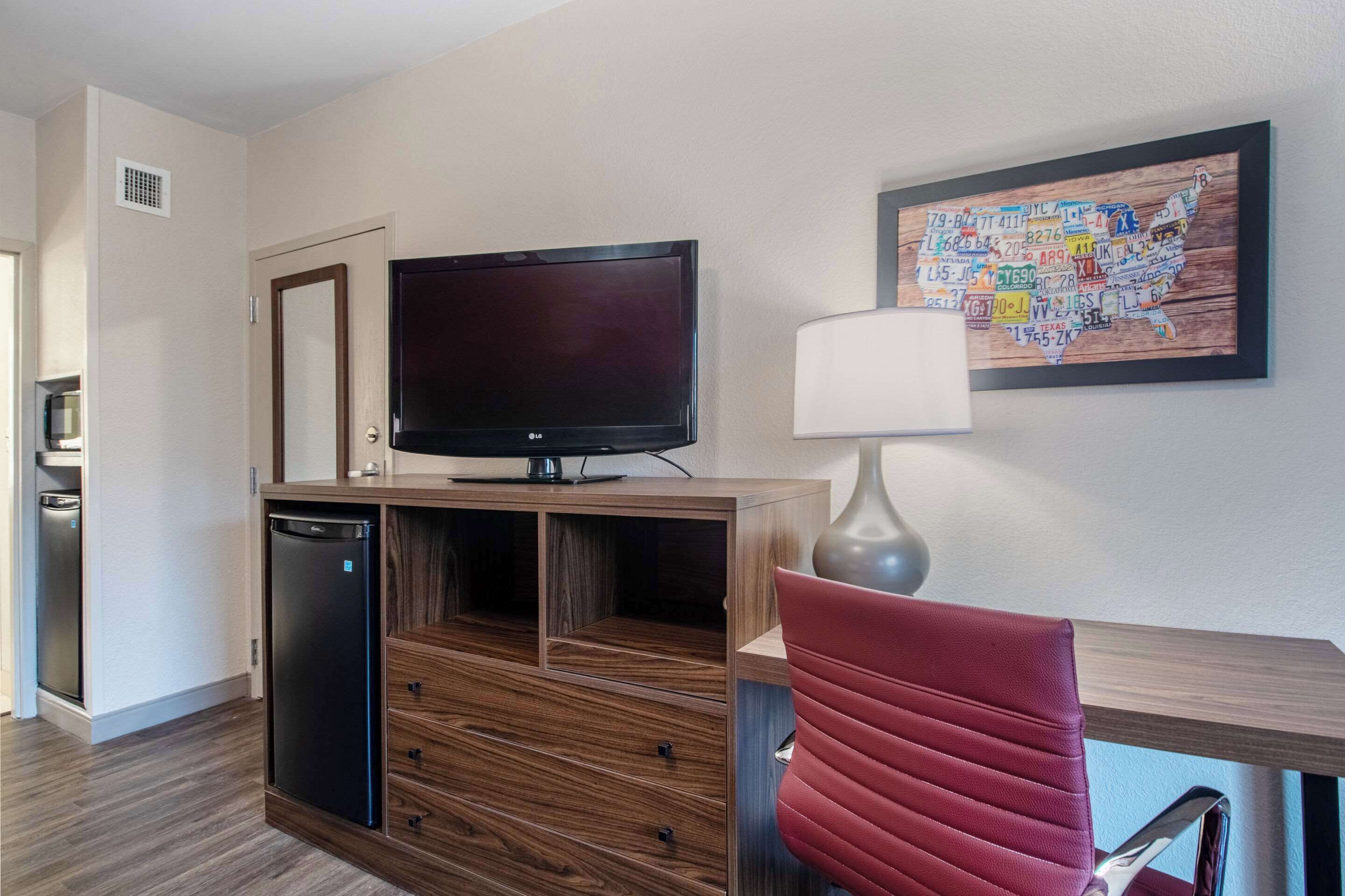 A hotel room with a wooden entertainment unit, a flat-screen TV, a red chair, and a wall map of the USA.